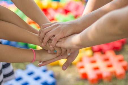 mains d'enfants réunies au centre avec pièces de couleurs en arrière plan