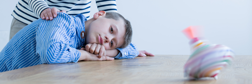 Jeune enfant autiste avec sa tête couchée sur une table et qui regarde une toupie