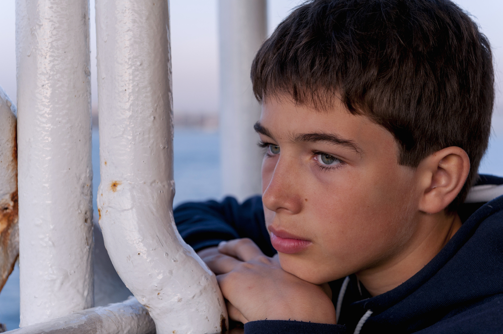 Jeune garçon brun autiste devant des tuyaux blancs qui regarde vers la gauche