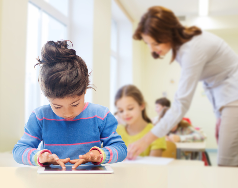 Education autisme Petite fille brune autiste qui consulte une tablette tactile avec une éducatrice et un autre enfant en arrière plan