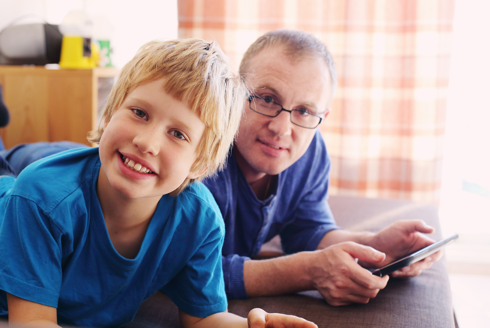 Garçonnet blond autiste avec son père qui consulte une tablette