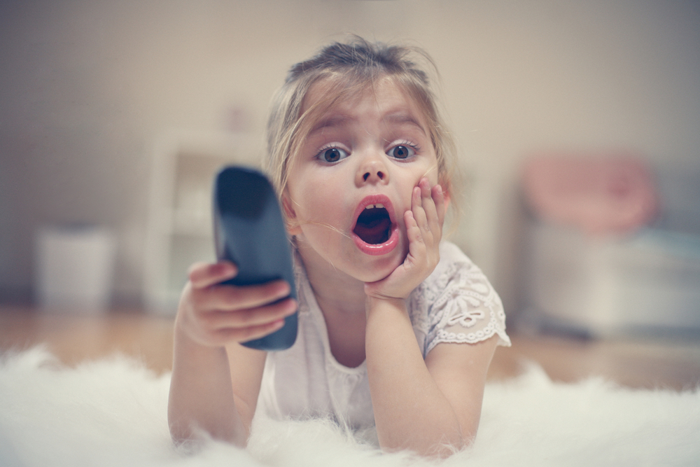 Petite fille blonde avec l'air étonne et une télécommande à la main