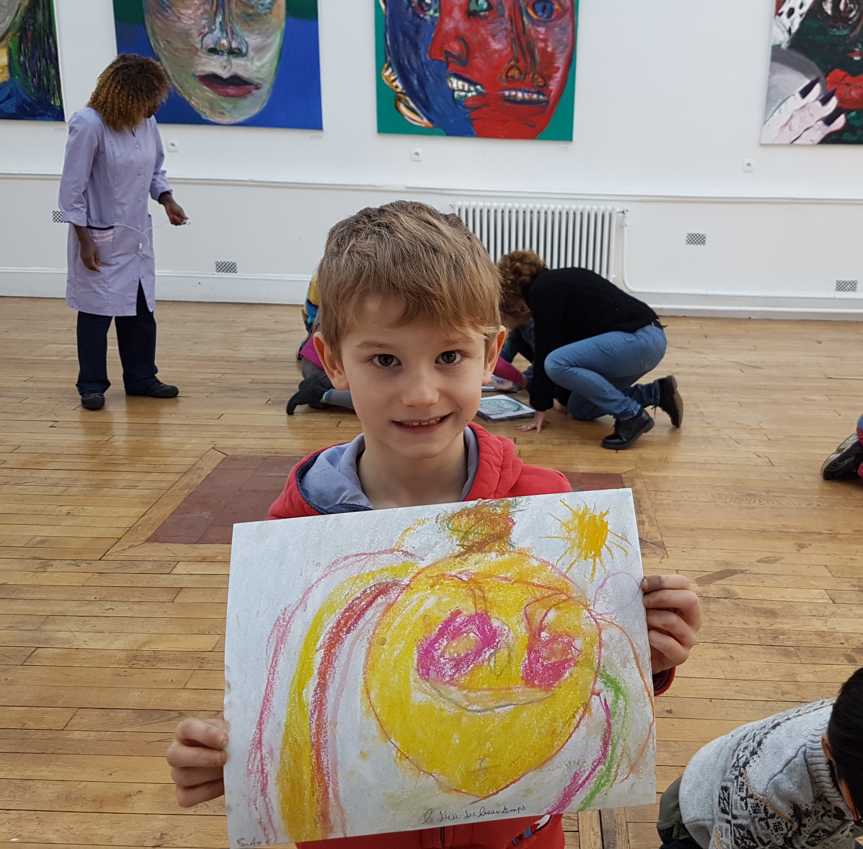 Enfant blond dans des locaux scolaires présentant son dessin au premier plan