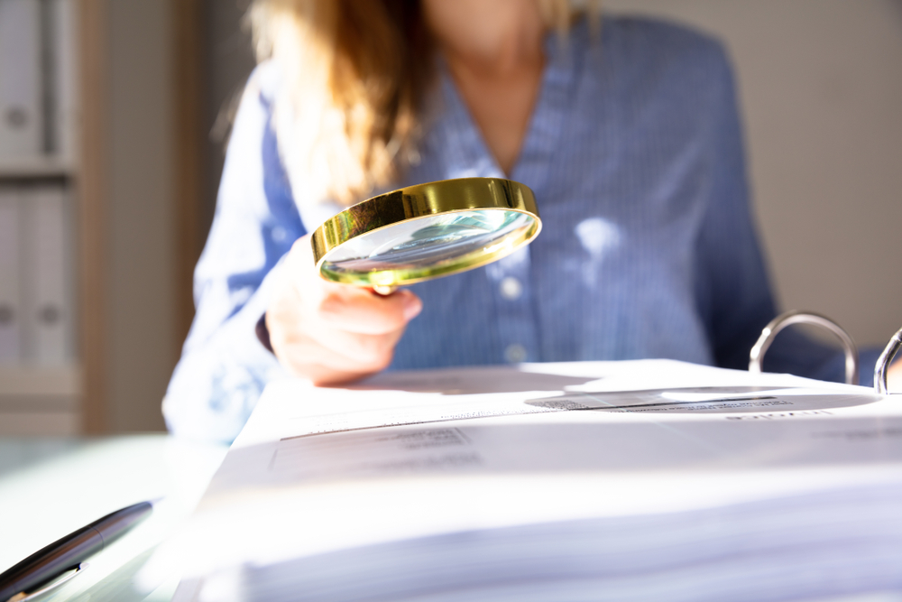 une femme en second plan consulte un document avec une loupe