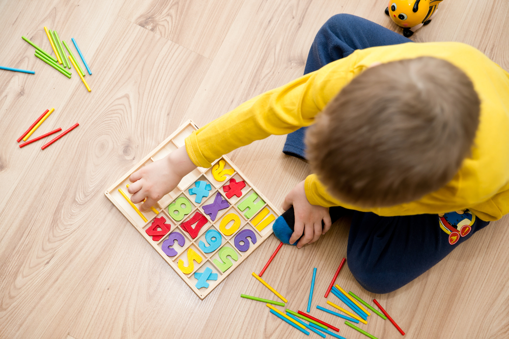 enfant pris de haut qui joue au sol avec des lettres de couleurs