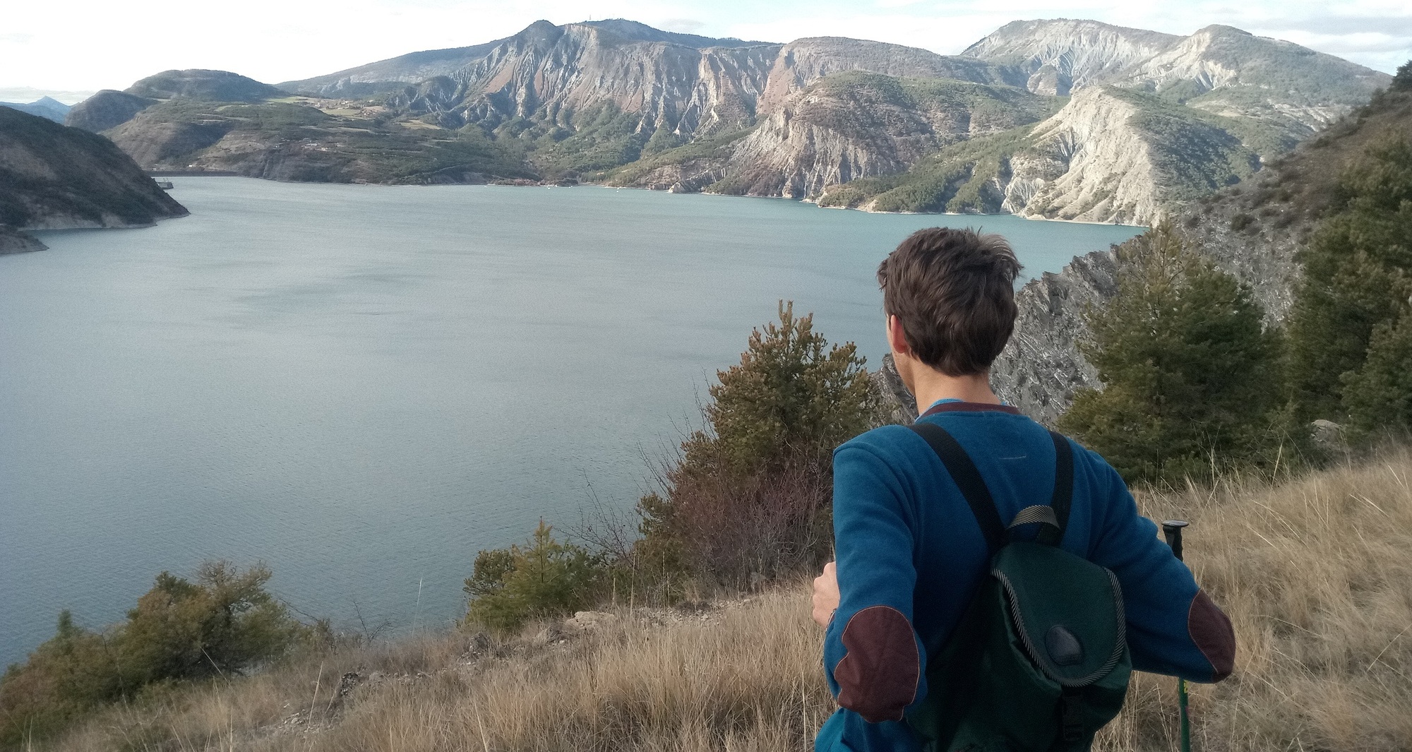 Jeune homme de dos qui regarde devant lui un paysage de montagne avec un lac