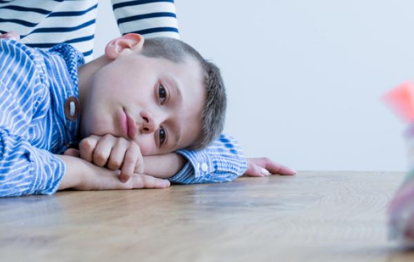 Jeune enfant autiste avec sa tête couchée sur une table et qui regarde une toupie
