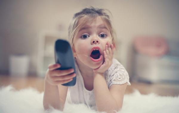 Petite fille blonde avec l'air étonné et une télécommande à la main