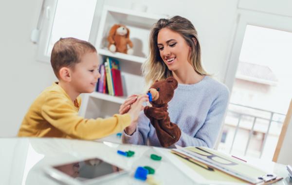 Educatrice avec une marionnette de nounours qui s'adresse à un jeune garçon autiste