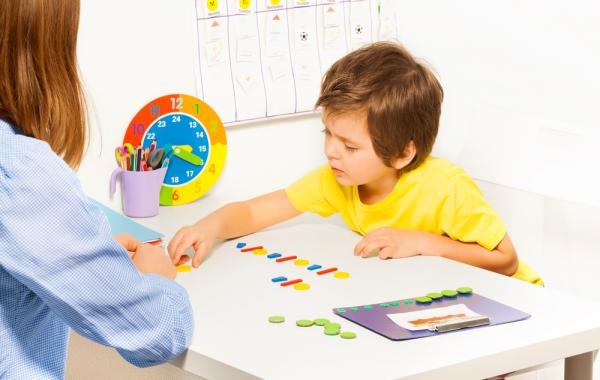 Jeune enfant autiste devant des pièces de couleurs et à coté d'un timer