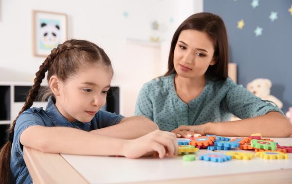 Éducatrice et fillette autiste cote à cote devant des pièces de jeu