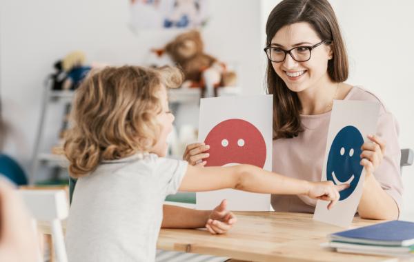 Éducatrice qui présente des pictogrammes à un enfant blond autiste de dos