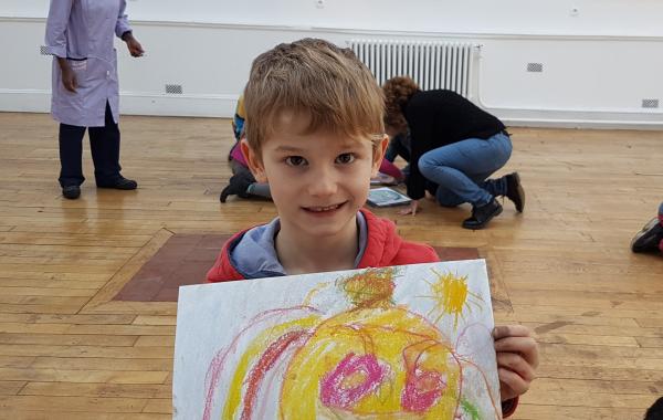 Enfant blond dans des locaux scolaires présentant son dessin au premier plan