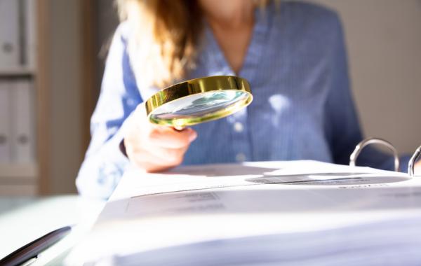 une femme en second plan consulte un document avec une loupe