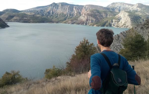 Jeune homme de dos qui regarde devant lui un paysage de montagne avec un lac