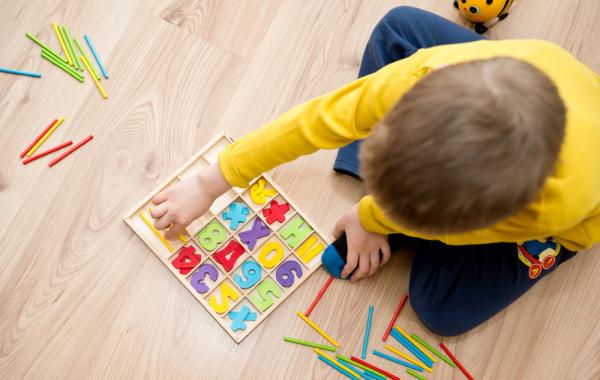 Enfant autiste pris de haut et assis au sol devant des lettres de couleurs