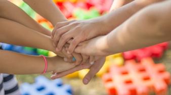mains d'enfants réunies au centre avec pièces de couleurs en arrière plan
