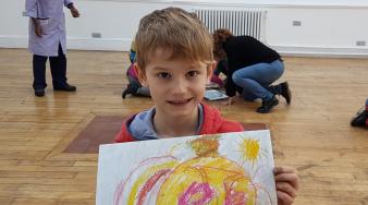 Enfant blond dans des locaux scolaires présentant son dessin au premier plan