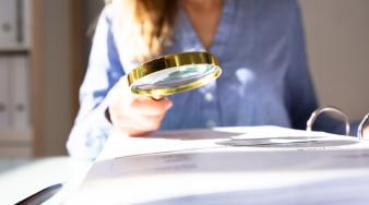 une femme en second plan consulte un document avec une loupe