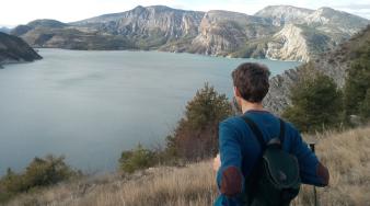 Jeune homme de dos qui regarde devant lui un paysage de montagne avec un lac