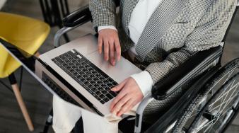 personne non identifiée positionnée dans un fauteuil roulant qui regarde un ordinateur portable