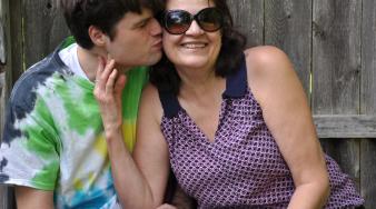 photo d'un jeune homme à côté de sa mère qui lui fait un baiser sur la joue