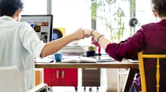 deux jeunes adultes de dos assis à un bureau se faisant un check